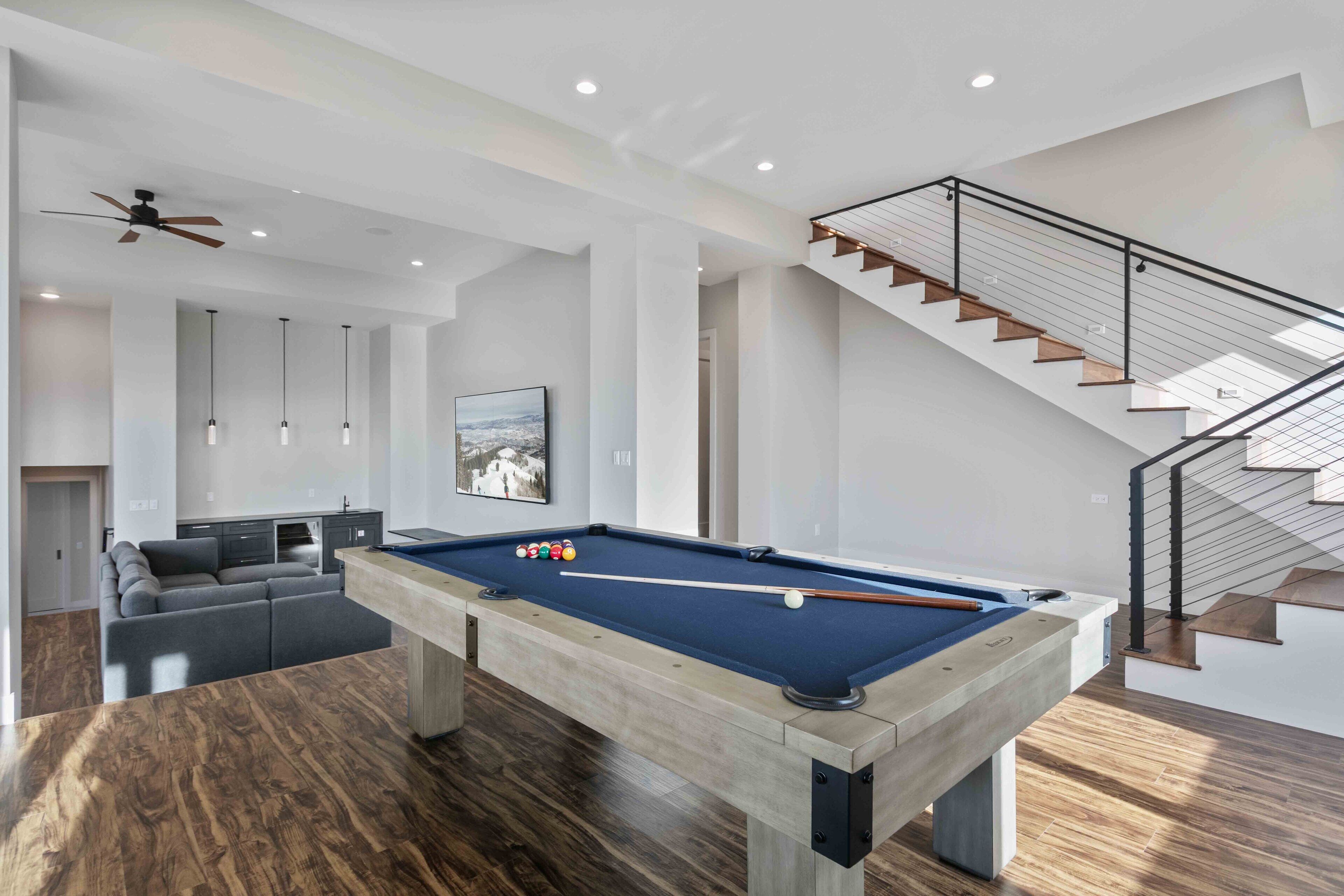 Un salon moderne avec une table de billard, un canapé et un escalier.