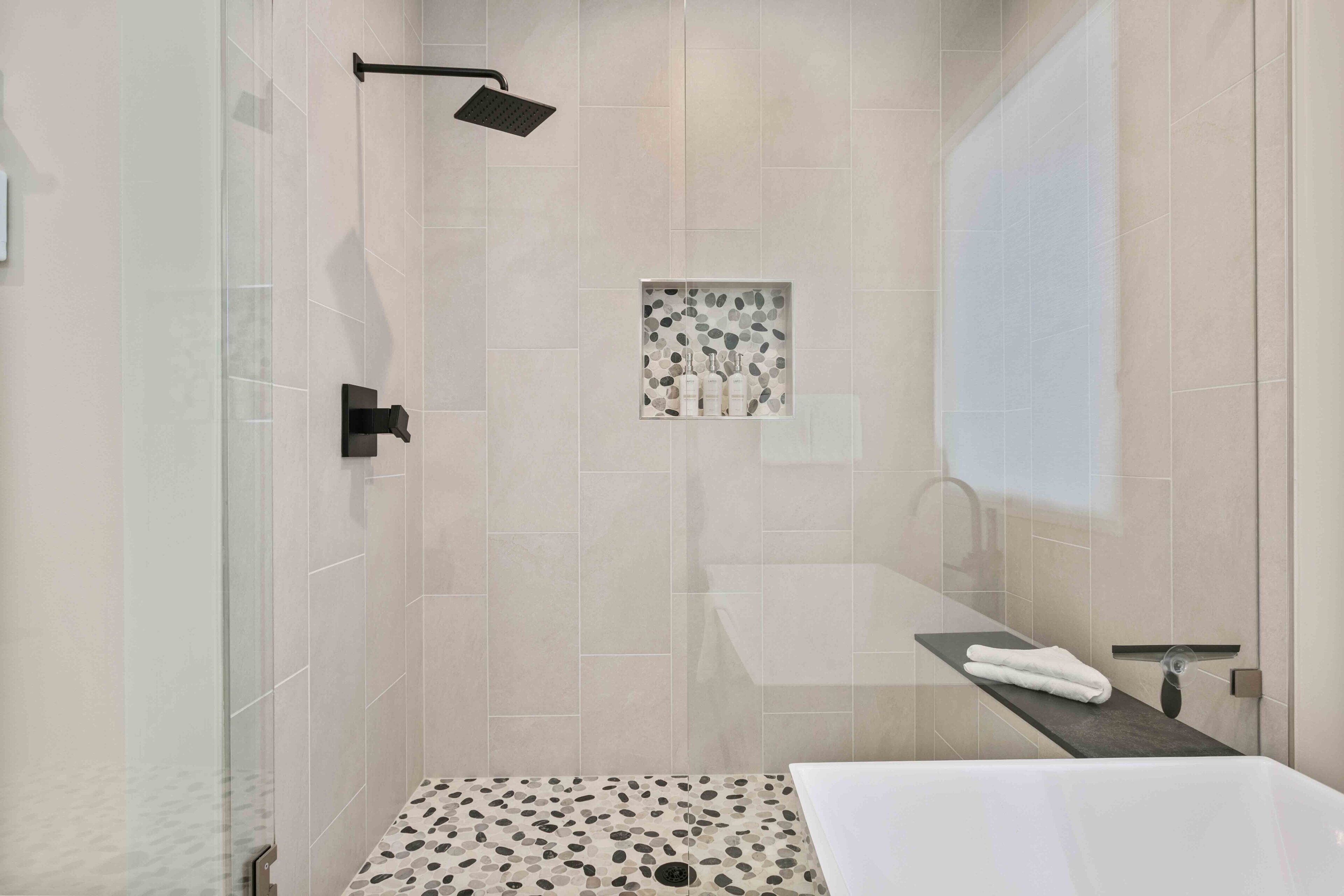 Ein modernes Badezimmer mit einer begehbaren Glasdusche, einer freistehenden Badewanne und einem Waschtisch mit Handtuchhalter.