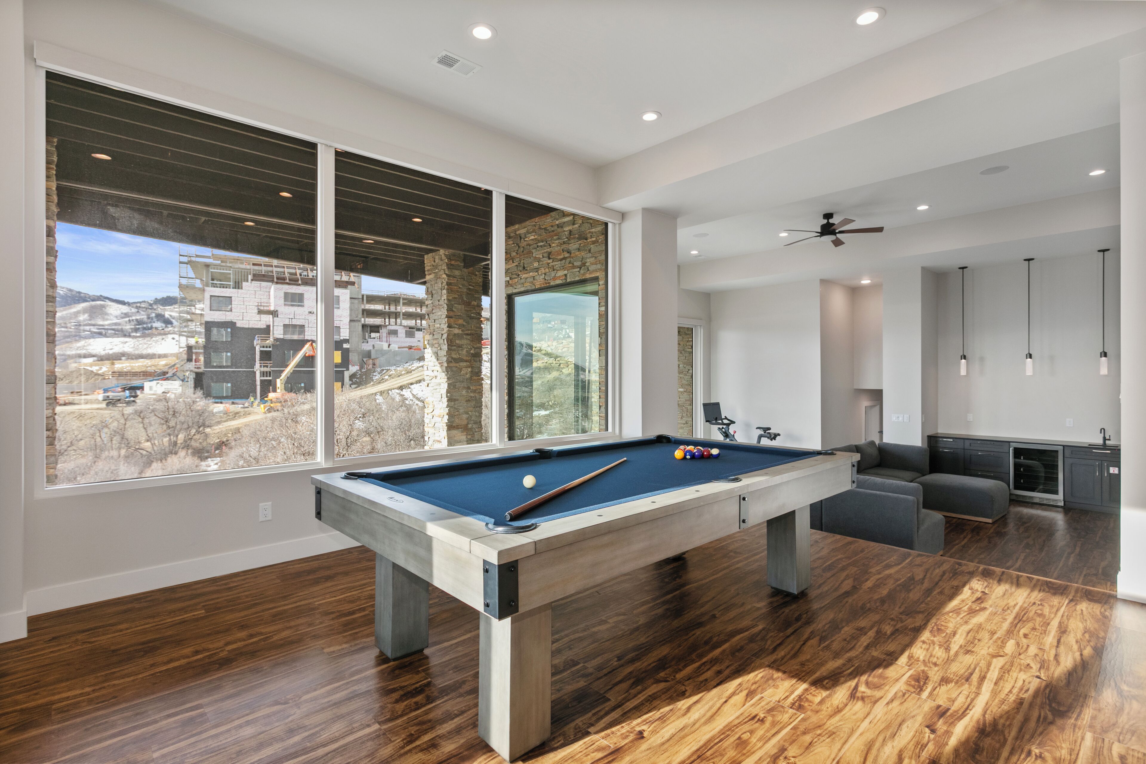 A modern living room with a pool table, large windows, and a view of a building under construction.