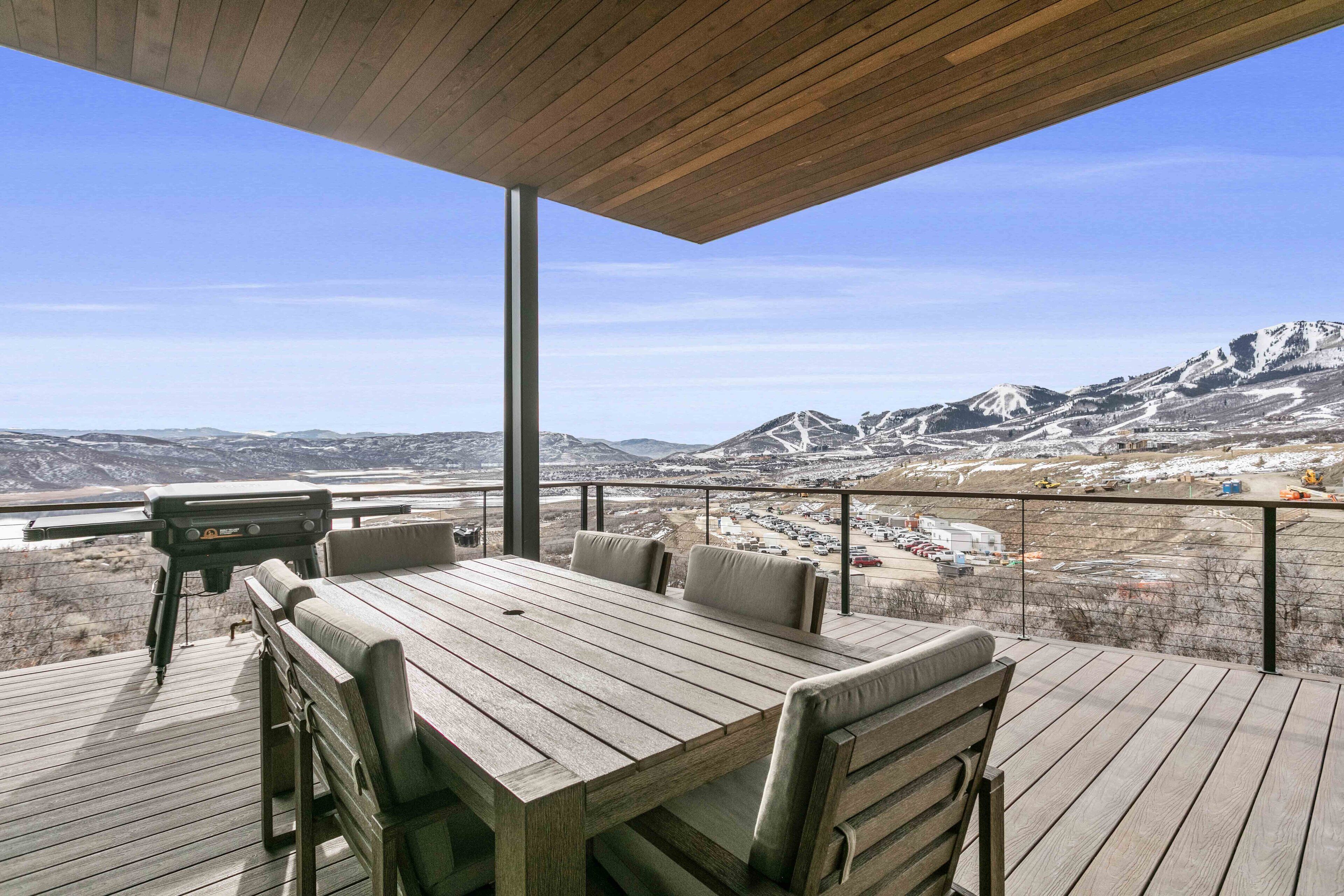 En træterrasse med et bord og stole, der kigger ud over et bjergrigt landskab.