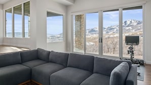 Una sala de estar moderna con un sofá seccional gris, ventanas amplias con vista a las montañas y una pared de acento de piedra.