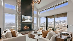Un salón amplio con chimenea, ventanas grandes y vistas a un paisaje montañoso.
