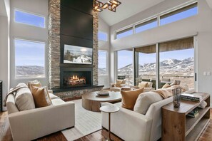 A spacious living room with a fireplace, large windows, and a view of a mountainous landscape. - Easy East Village Ski Access Hot Tub 5br 5 Bedroom Home (Heber City)
