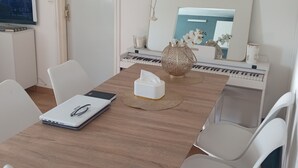 A dining area with a wooden table, white chairs, a clock, a computer setup, and a TV on a stand. - Free room/parking and bus in front (Amiens)