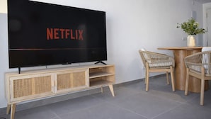 A modern living room with a large flat-screen TV mounted on a wall, a wooden TV stand, wicker chairs, and a small table with a plant. - Ap2147 in Denia With 2 Bedrooms and 1 Bathrooms (Denia)