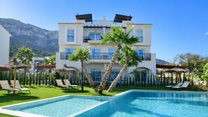 A poolside view of a hotel with a large pool, palm trees, and a mountain in the background. - Ap2147 in Denia With 2 Bedrooms and 1 Bathrooms (Denia)