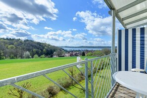 A balcony with a view of a green field and a lake, metal railing, and a table. - Deluxe Apartment with Lake View K3 203 (Spalt)