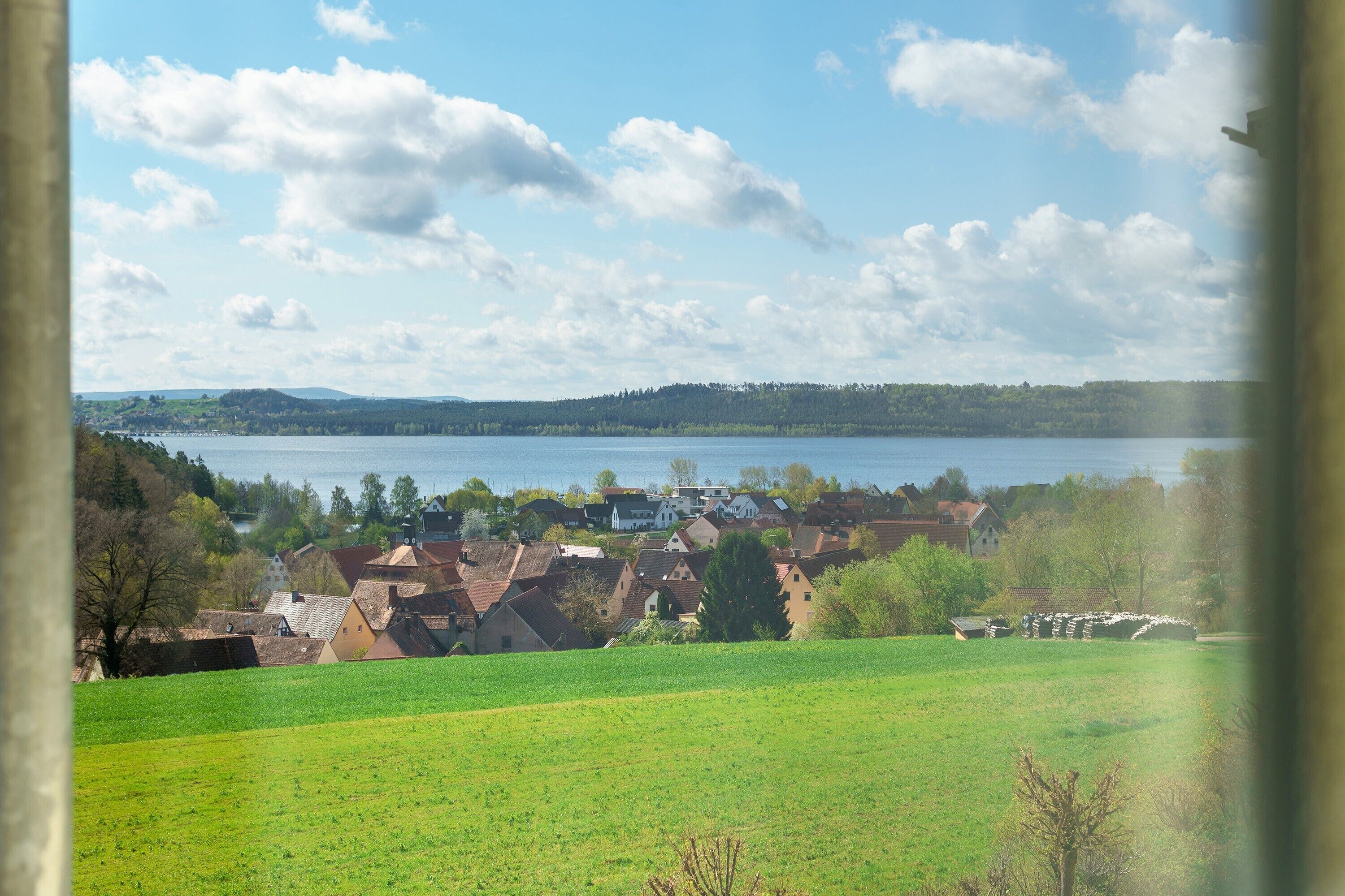 Maaseutumaisema, jossa on järvi, taloja ja avoimia peltoja.