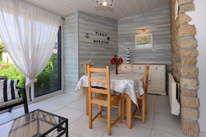 A dining area with a table set for four, a chair with a striped pillow, a vase with red flowers, and a wall with nautical-themed decor.