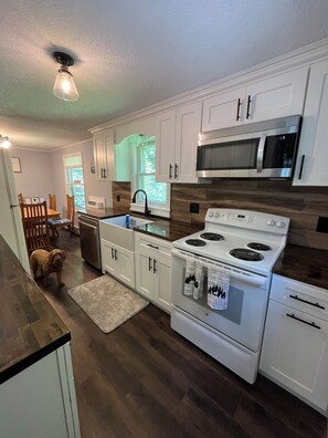 A modern kitchen with white cabinets, a stainless steel microwave, a white stove, and a wooden floor. - Lovely 4-bedroom Stratton - Mt. Snow Getaway (Wardsboro)
