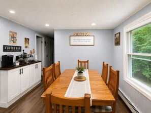 A dining area with a wooden table, chairs, a coffee bar, and a kitchen in the background. - Lovely 4-bedroom Stratton - Mt. Snow Getaway (Wardsboro)