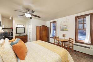 A bedroom with a bed, a desk, a chair, a wardrobe, a ceiling fan, a window with curtains, and a radiator.