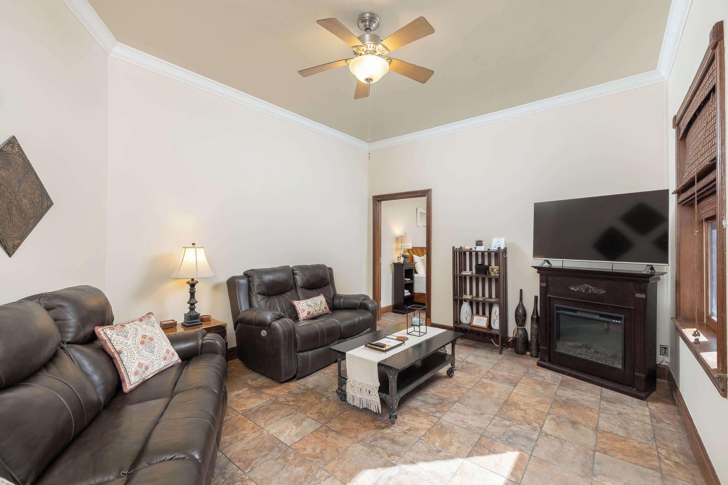 A living room with a dark leather sofa, a coffee table, a fireplace, and a ceiling fan.