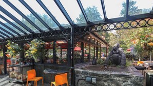 Un café al aire libre con un muro de piedra, sillas anaranjadas y una estatua.