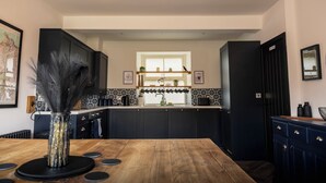 Una cocina moderna con armarios oscuros, una mesa de madera e iluminación colgante.