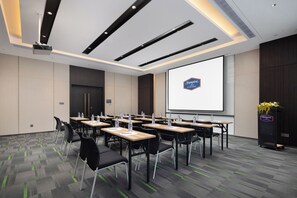 A conference room with tables, chairs, a projector screen, and a logo on the wall. - Hampton by Hilton Ningde Lithium Electricity Town (Ningde)
