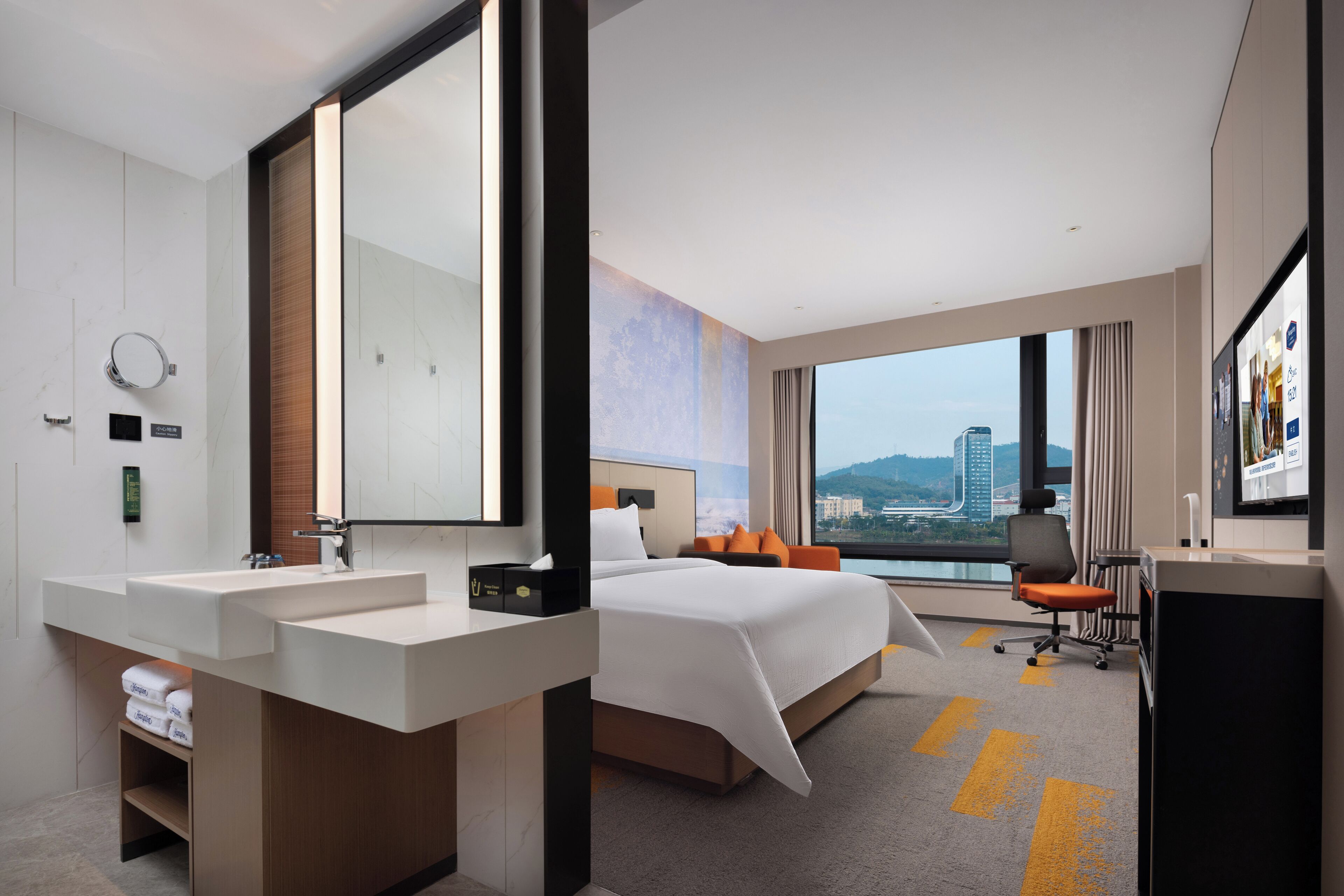 Habitación de hotel moderna con una cama grande, lavamanos doble, un espejo amplio y vistas a un paisaje urbano.