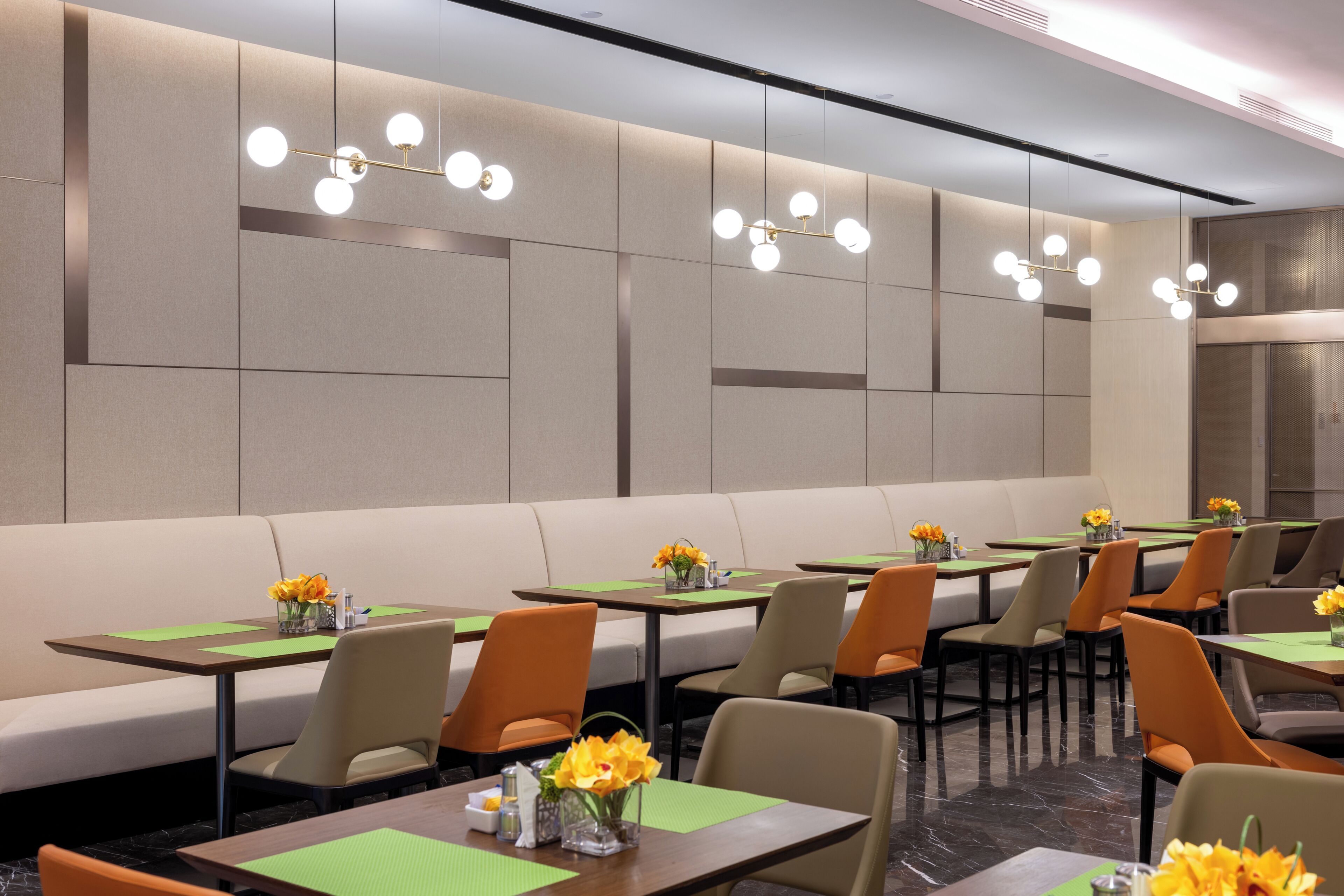 A modern dining area with booths and tables, each with a vase of flowers and green placemats.