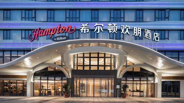 A modern hotel entrance with a prominent sign, large glass doors, and a curved overhang structure. - Hampton by Hilton Ningde Lithium Electricity Town (Ningde)