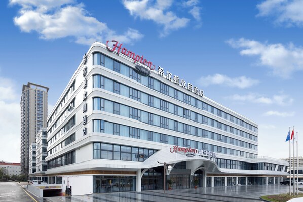 A modern hotel with a prominent 'Hampton' sign, multiple floors, and a covered entrance area.