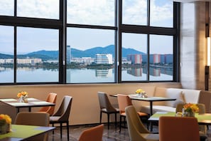 A restaurant with a view of a body of water and mountains, featuring tables and chairs arranged for dining. - Hampton by Hilton Ningde Lithium Electricity Town (Ningde)