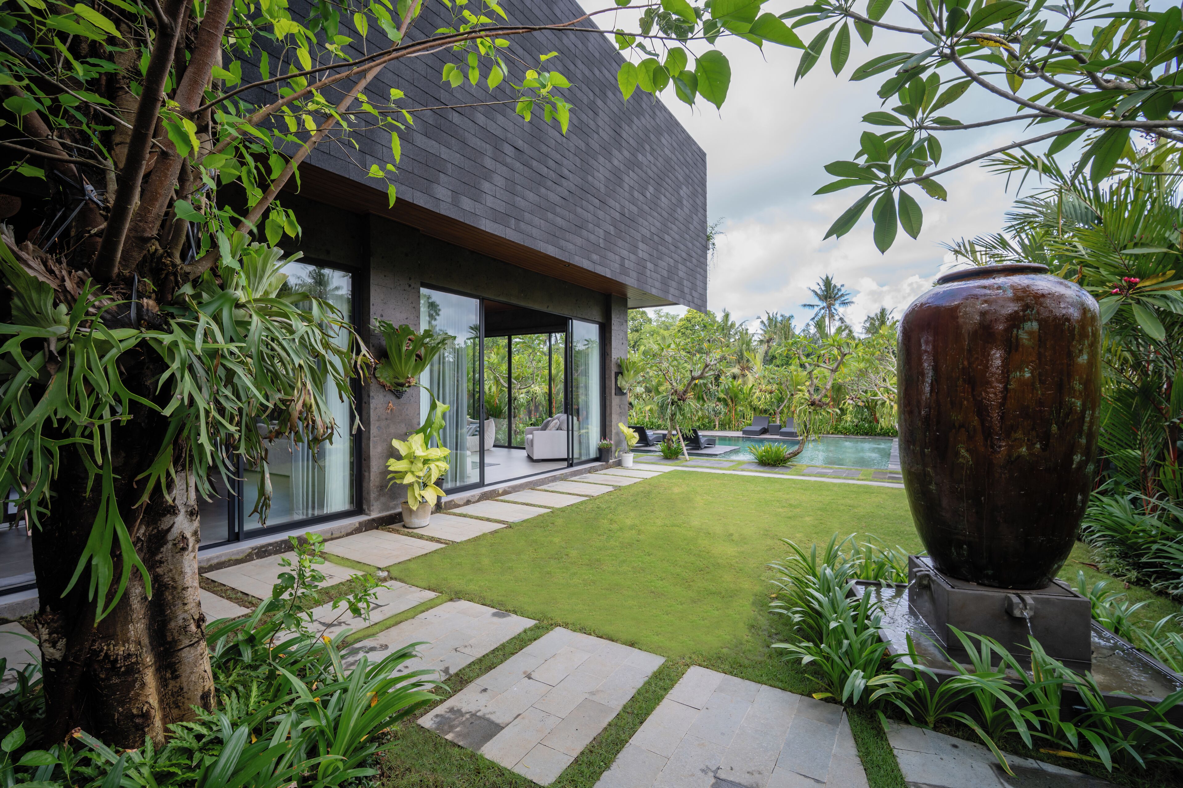 A modern house with a large glass window, a stone pathway, and a well-maintained lawn.