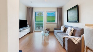 A living room with a sofa, a glass coffee table, a TV, and a window with curtains. - Dog-Friendly Apartment H1 005 (Spalt)