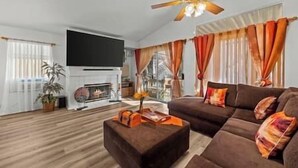 Ein Wohnzimmer mit Kamin, einer Sofagarnitur, einem Flachbildfernseher und einem Deckenventilator.