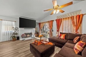 Ein Wohnzimmer mit Kamin, einer Sofagarnitur, einem Flachbildfernseher und einem Deckenventilator.