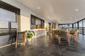 A spacious room with a high ceiling, large windows, a bar area, and a seating arrangement. - Waikiki Coastal Retreat | Walk to Beach | Pet Friendly (Waikiki)