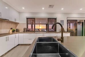 A modern kitchen with a large island, white cabinetry, and a view of the sunset through large windows. - Waikiki Coastal Retreat | Walk to Beach | Pet Friendly (Waikiki)