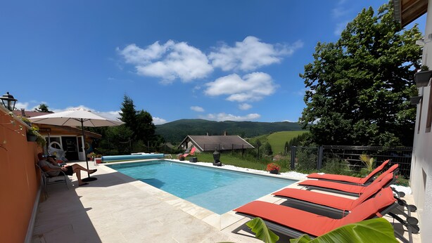 Una piscina con sillas de descanso, una planta en maceta y vistas a una casa y colinas.
