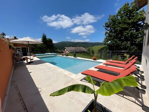 A swimming pool with lounge chairs, a potted plant, and a view of a house and hills. - Bed and Breakfast 'La Chambre De Jaxel' with Mountain View, Shared Pool and Wi-Fi (Saint-Martin-en-Vercors)