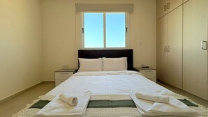 Een slaapkamer met een bed, nachtkastje, kledingkast en raam.