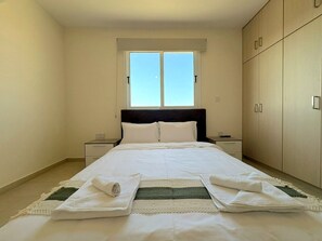 A bedroom with a bed, a nightstand, a wardrobe, and a window. - Sunrise Palette Suites - 2Bedroom 6' away from sea (Xylofagou)