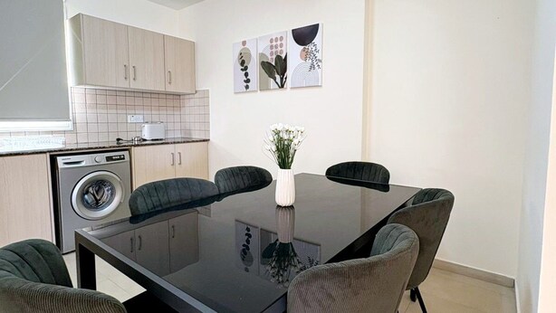 Een moderne keuken met een ingebouwde wasmachine, een eettafel met zes stoelen en een kleine potplant.