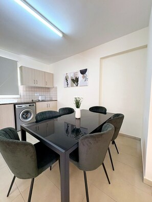 Une cuisine moderne équipée d’un lave-linge intégré, d’une table à manger avec six chaises et d’une petite plante en pot.