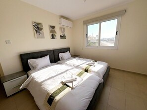 Une chambre à coucher avec un lit double, une table de chevet, une fenêtre donnant sur la ville et des œuvres d’art murales.