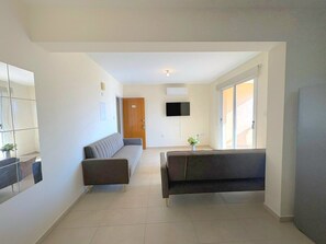 A modern living room with a sofa, a coffee table, and a flat-screen TV mounted on the wall. - Sunrise Palette Suites - 2Bedroom 6' away from sea (Xylofagou)