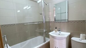 Een badkamer met een bad, een douche met glazen wanden, een wastafel en een toilet.