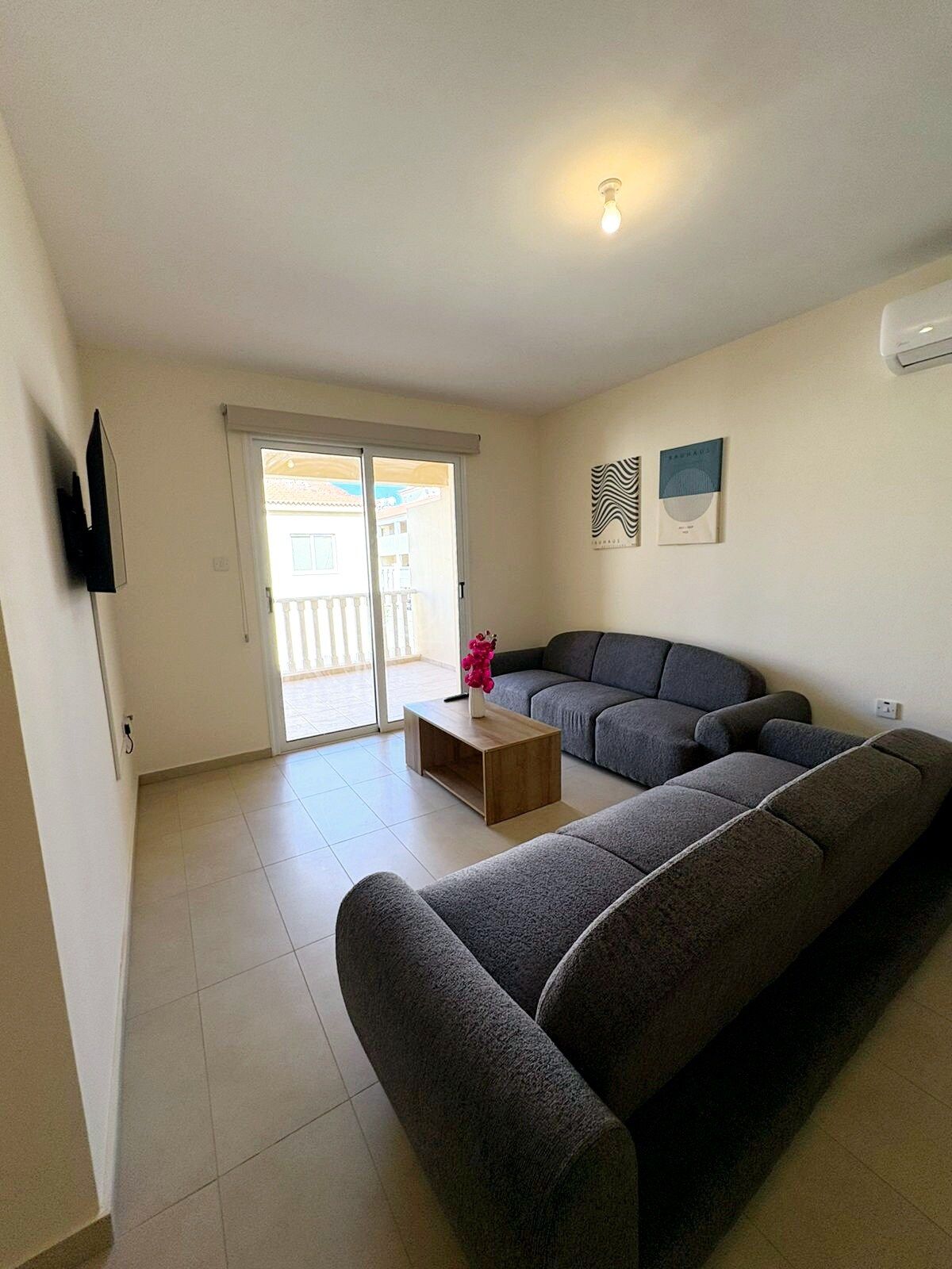 A living room with a grey sectional sofa, a wooden coffee table, and a television mounted on the wall.