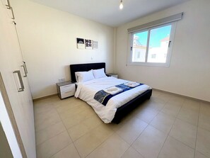 A bedroom with a bed, bedside tables, a window, and a door. - Sunrise Palette Suites - 1bedroom 6' way from sea (Xylofagou)