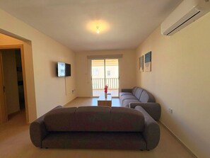 A living room with a sofa, a television, and a balcony with a view. - Sunrise Palette Suites - 1bedroom 6' way from sea (Xylofagou)