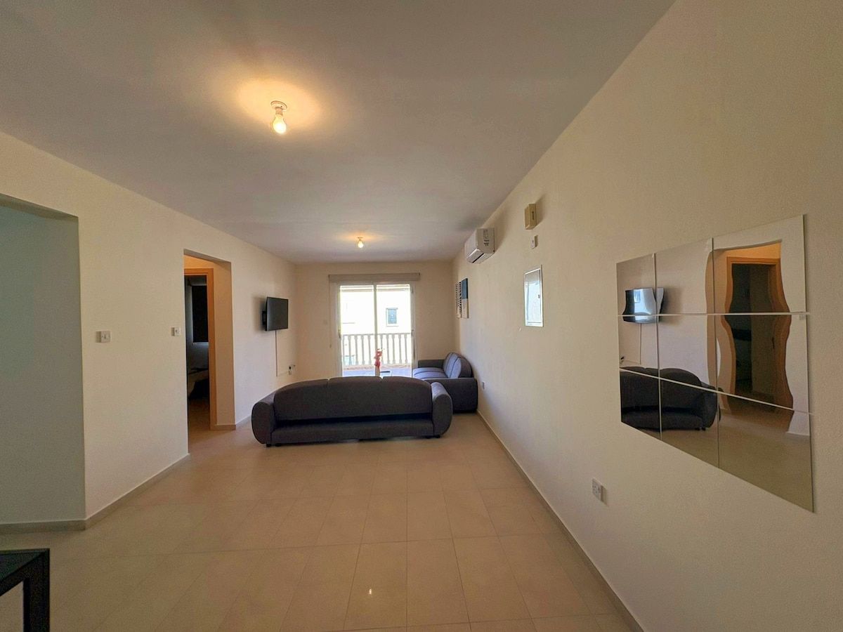 Un espacio habitable amplio con un sofá, un televisor y un espejo grande en la pared.