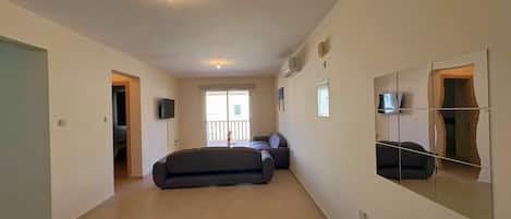A spacious living area with a sofa, a television, and a large mirror on the wall.