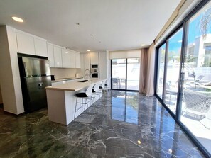 A modern kitchen with a central island, stainless steel appliances, and a large sliding glass door leading to an outdoor area. - Panorama Luxury Summer Villa (Paralimni)