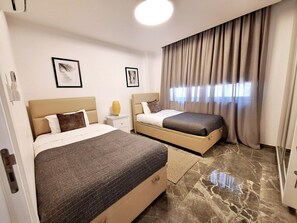 A hotel room with two beds, a nightstand, a lamp, and a window with curtains. - Panorama Luxury Summer Villa (Paralimni)