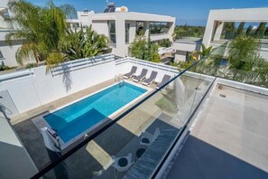 A rooftop swimming pool with lounge chairs, surrounded by modern buildings and greenery. - Panorama Luxury Summer Villa (Paralimni)