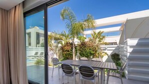 Ett modernt hotellrum med en glasdörr som leder ut till en balkong med pool, utomhusmöbler och frodig grönska.