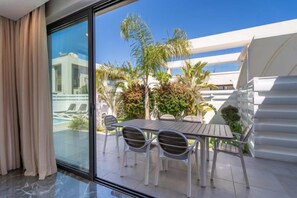 A modern hotel room with a glass door leading to a balcony with a pool, outdoor seating, and lush greenery. - Panorama Luxury Summer Villa (Paralimni)